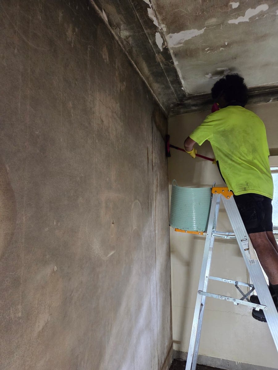 CleanUp Partners technician in respirator PPE on a ladder scrubbing floor-to-ceiling black mould off walls