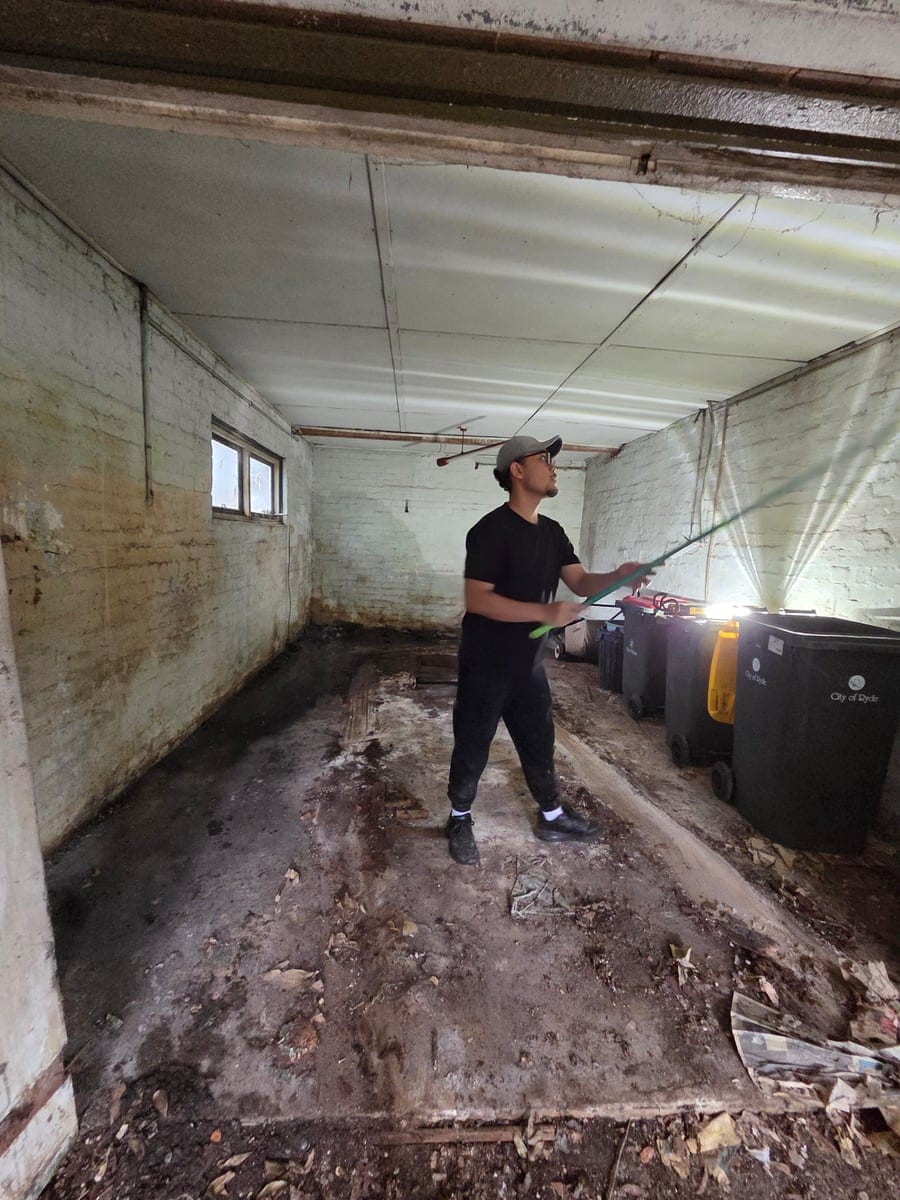 Technician pressure washing and sanitising a cleared garage and concrete floor